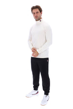A man modeling a white long-sleeve mock neck knit top and black jogger pants with white sneakers, standing against a solid white background.