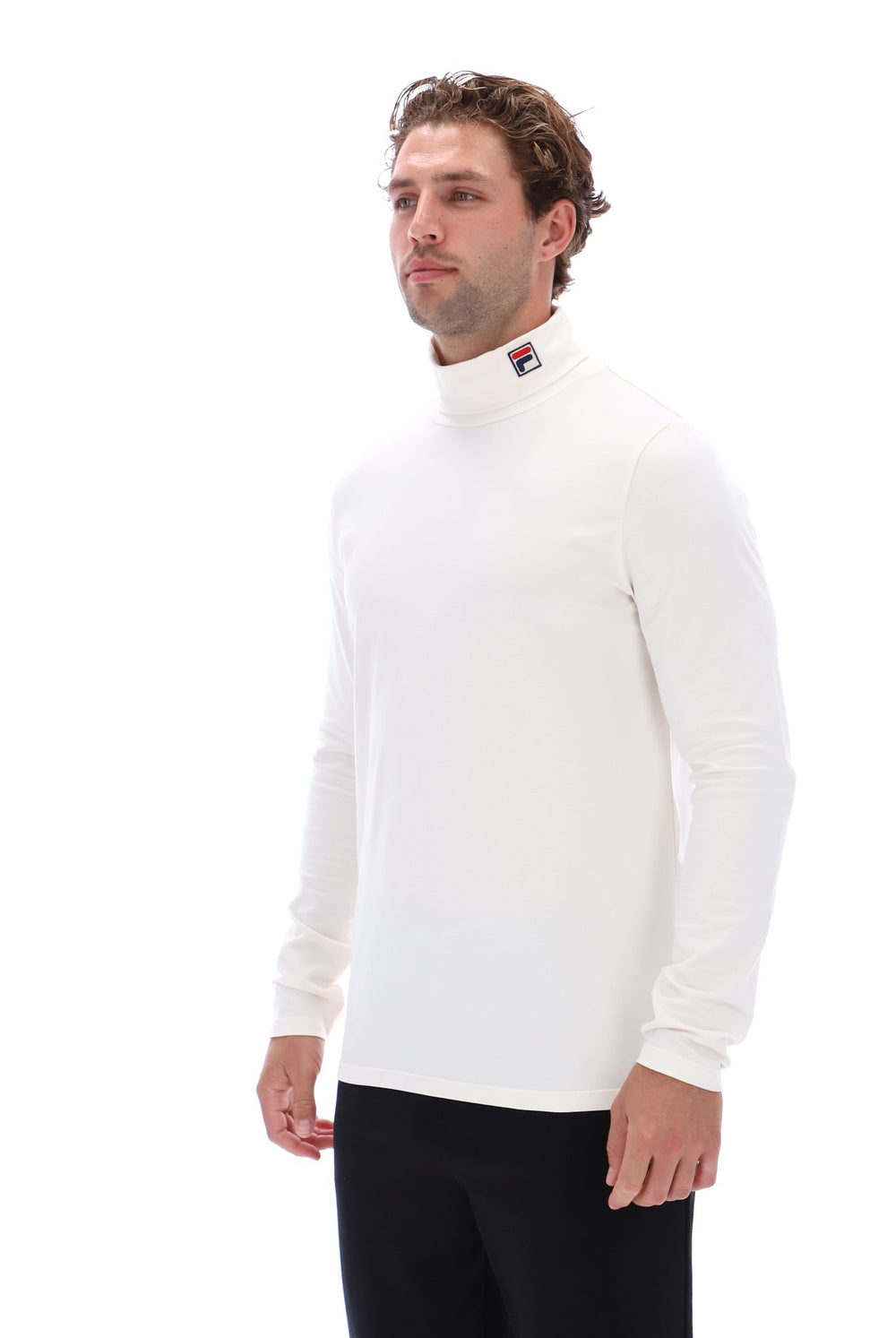 A man wearing a white long-sleeve mock neck turtleneck sweater with a small Fila logo on the collar, paired with black pants, photographed against a solid white background.
