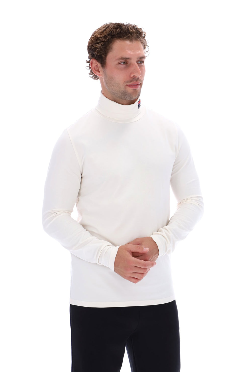 A man wearing a white long-sleeve mock neck turtleneck sweater and black pants, standing against a solid white background.
