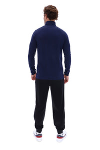 A man viewed from behind wearing a navy blue mock neck long-sleeve top, black sweatpants, and white sneakers with red and blue accents, set against a plain white background.