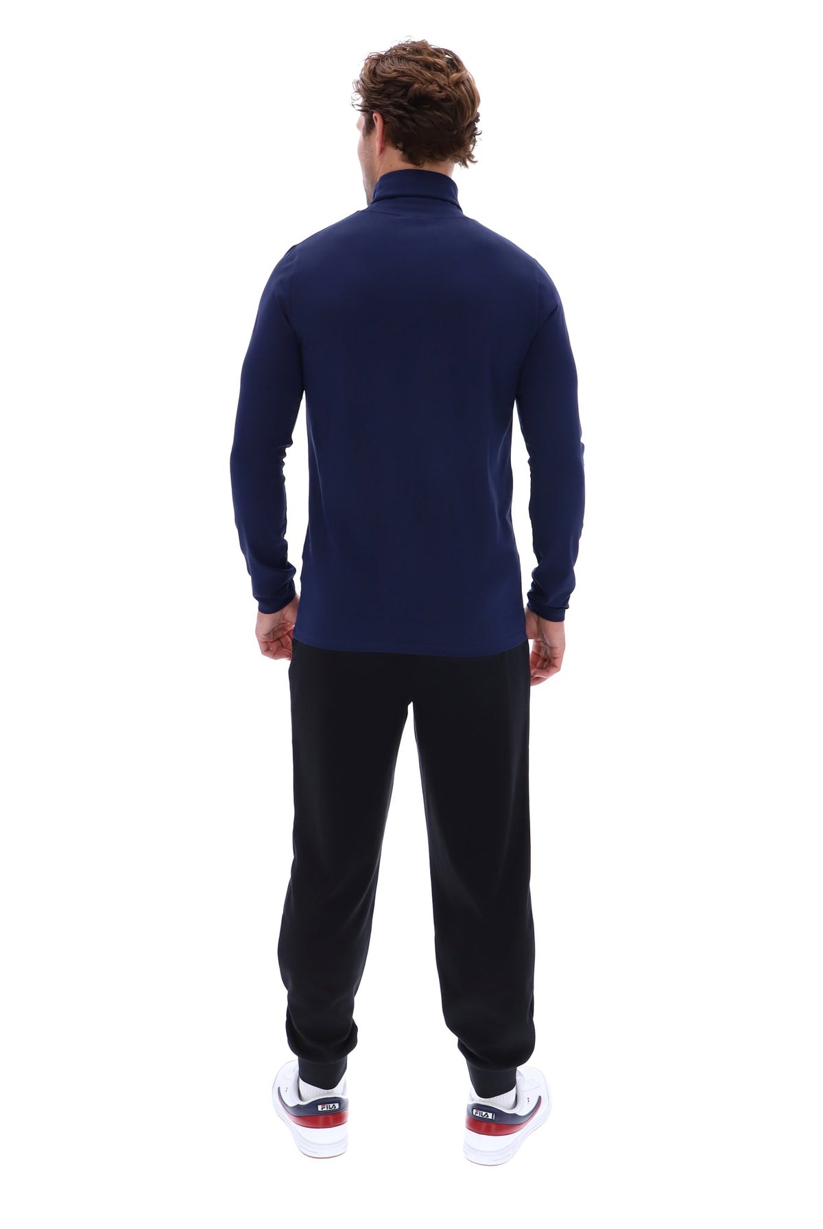 A man viewed from behind wearing a navy blue mock neck long-sleeve top, black sweatpants, and white sneakers with red and blue accents, set against a plain white background.