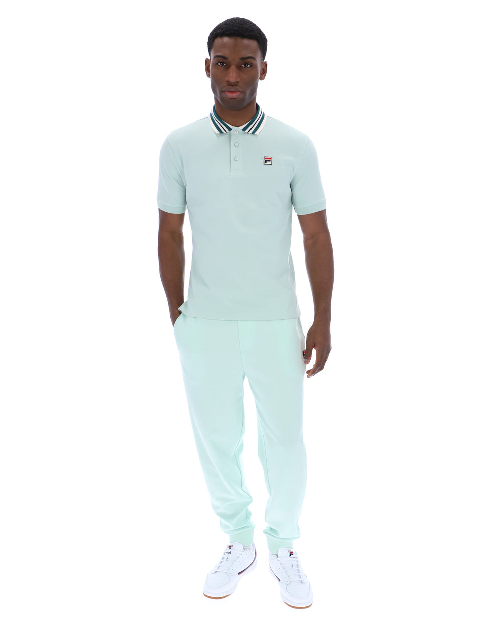 Man wearing a light green polo shirt with a small FILA logo on the chest, paired with matching joggers, against a white background