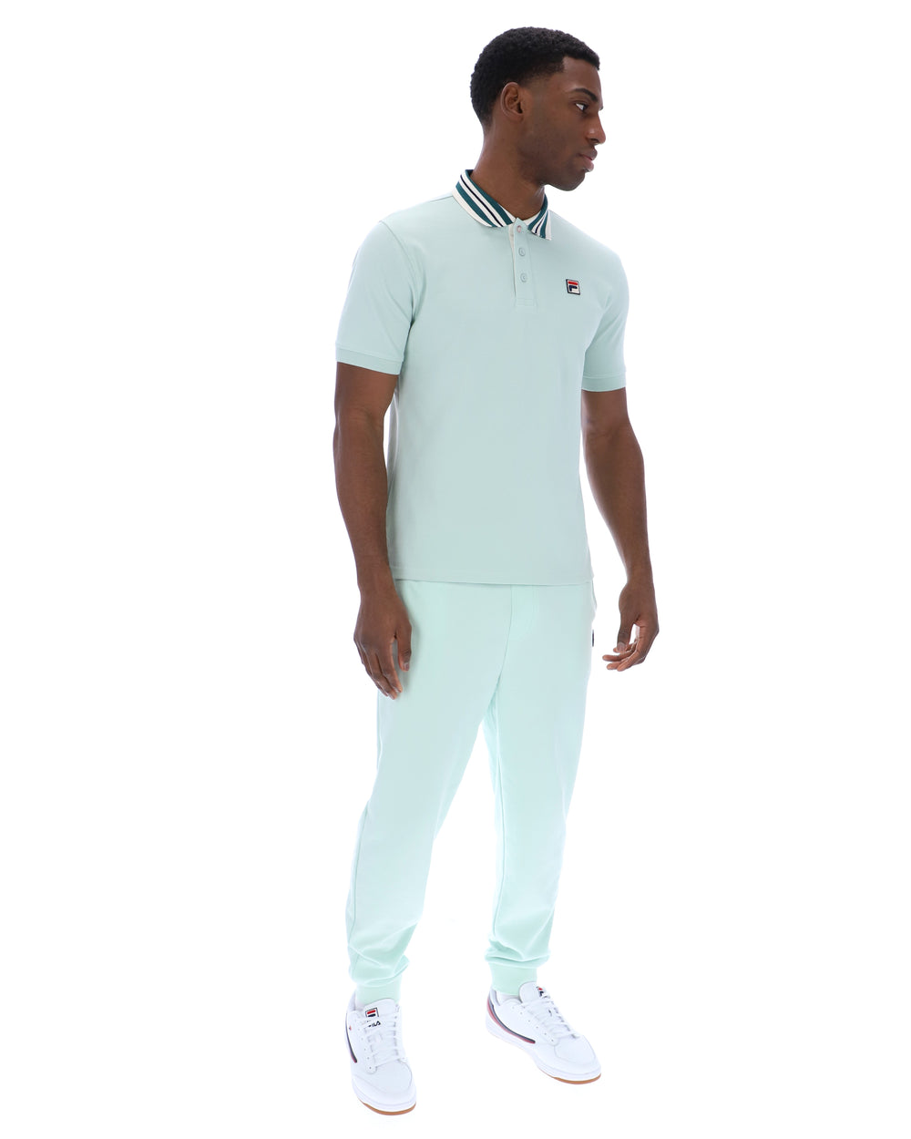 Man wearing a light green polo shirt with a small FILA logo on the chest, paired with matching joggers, against a white background