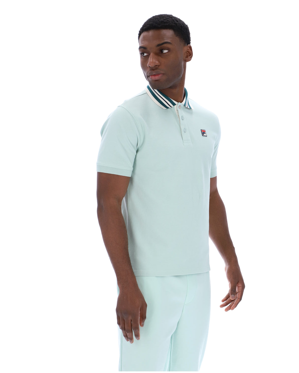 Man wearing a light green polo shirt with a small FILA logo on the chest, paired with matching joggers, against a white background