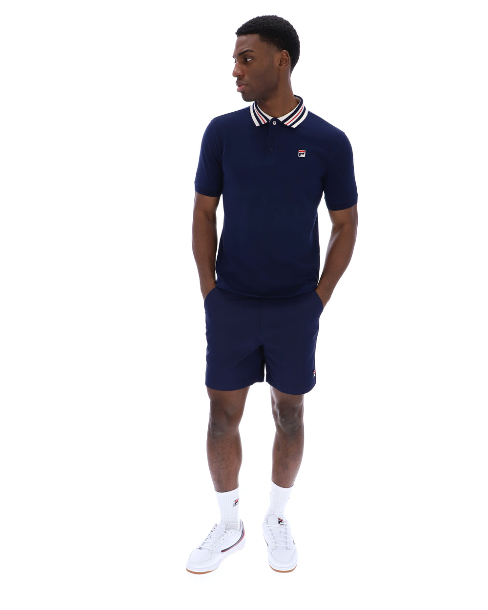 Man wearing a navy polo shirt and shorts with white accents on a white background