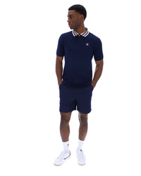 Man wearing a navy polo shirt and shorts with white accents on a white background