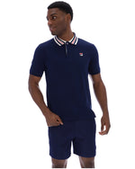 Man wearing a navy polo shirt and shorts with a visible brand logo on a white background