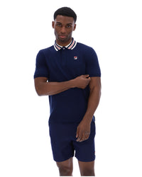 Man wearing a navy blue polo shirt and shorts set with a small logo on a white background