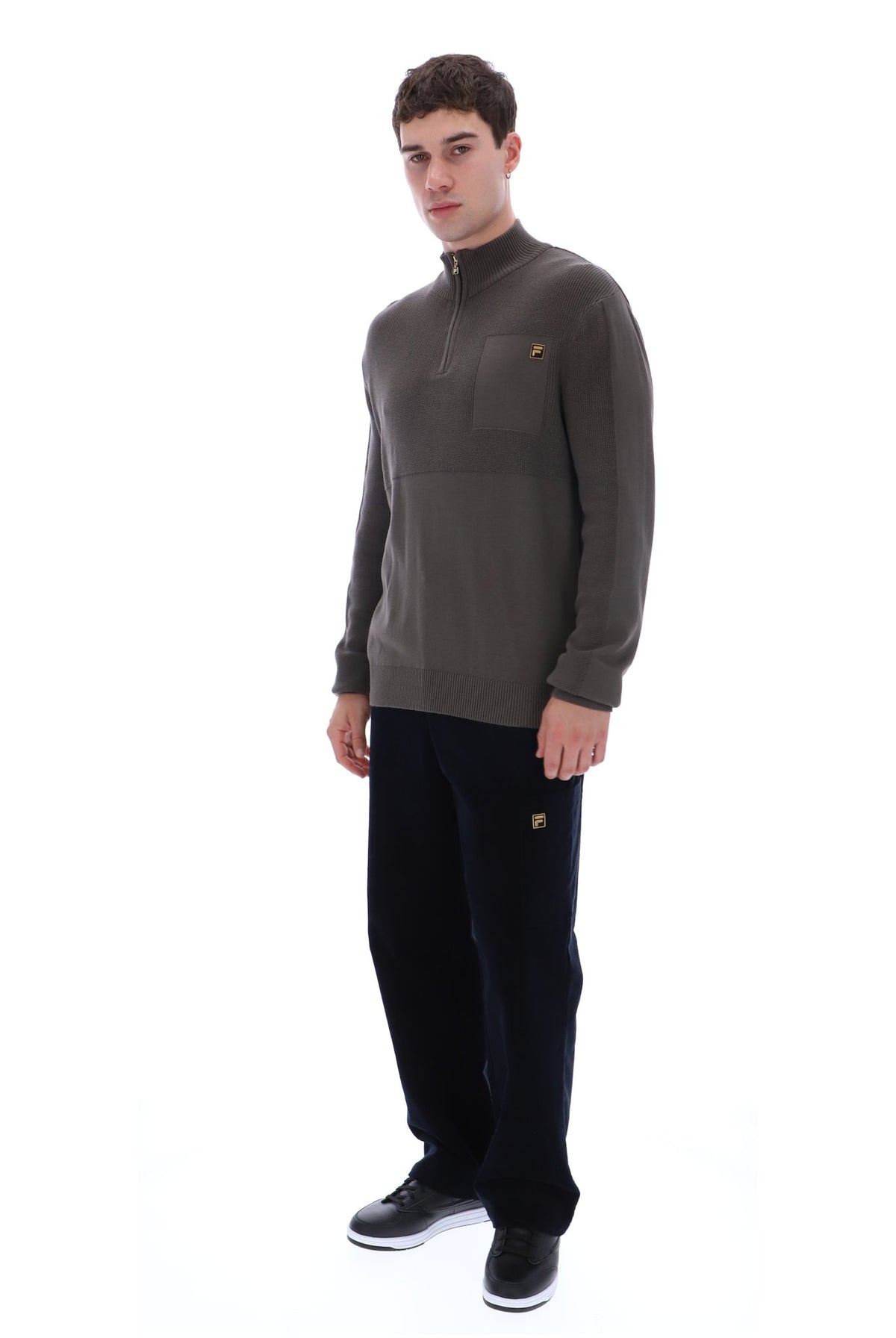 A man modeling a dark brown quarter-zip fleece pullover with a small embroidered logo on the left chest, paired with black sweatpants and black sneakers, against a solid white background.