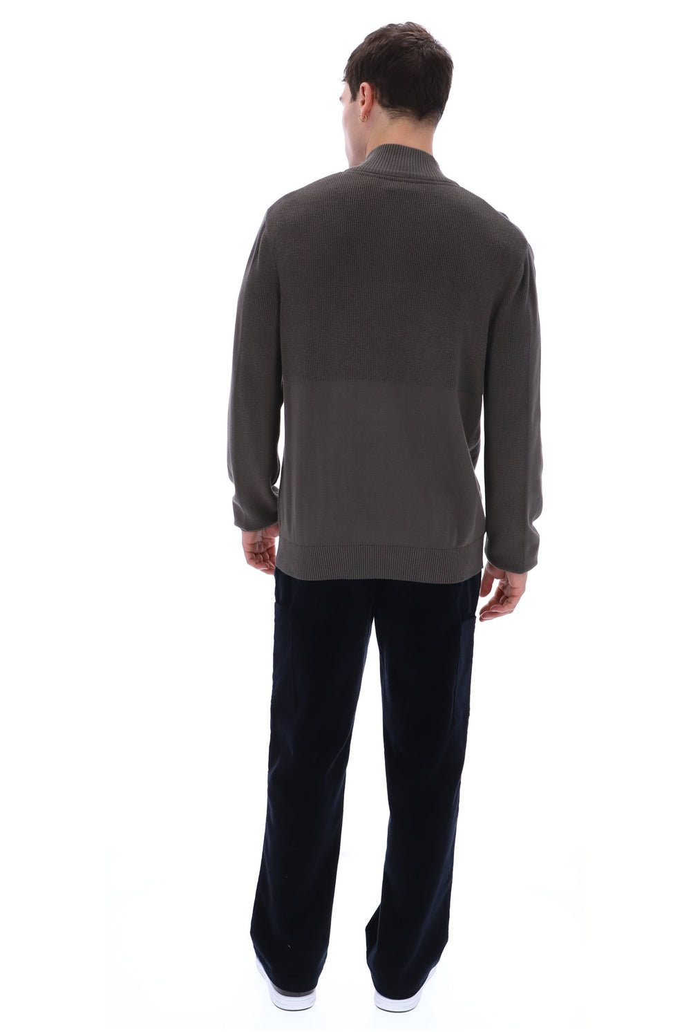 A man viewed from behind wearing a dark brown long-sleeve knit sweater and black trousers, standing against a plain white background.