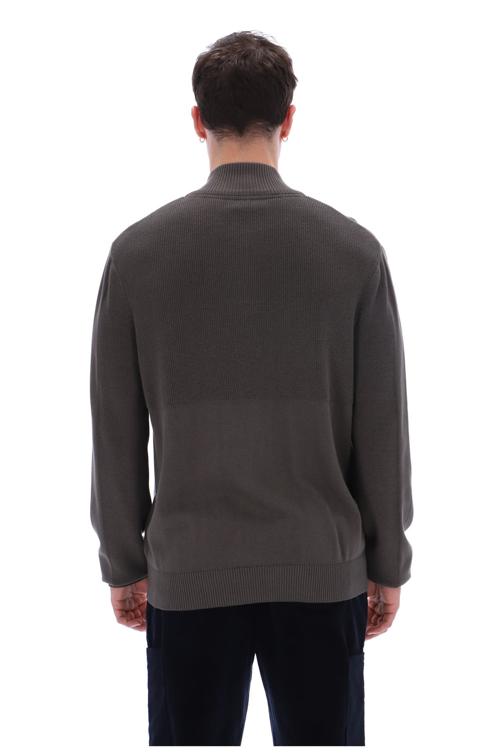 A man viewed from the back wearing a dark brown ribbed knit sweater and dark trousers against a plain white background.