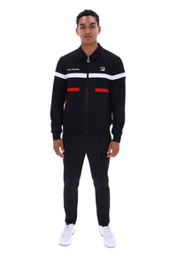 A man modeling a black FILA track suit with white and red stripe details on the chest and waist, paired with white sneakers, shot against a plain white background.