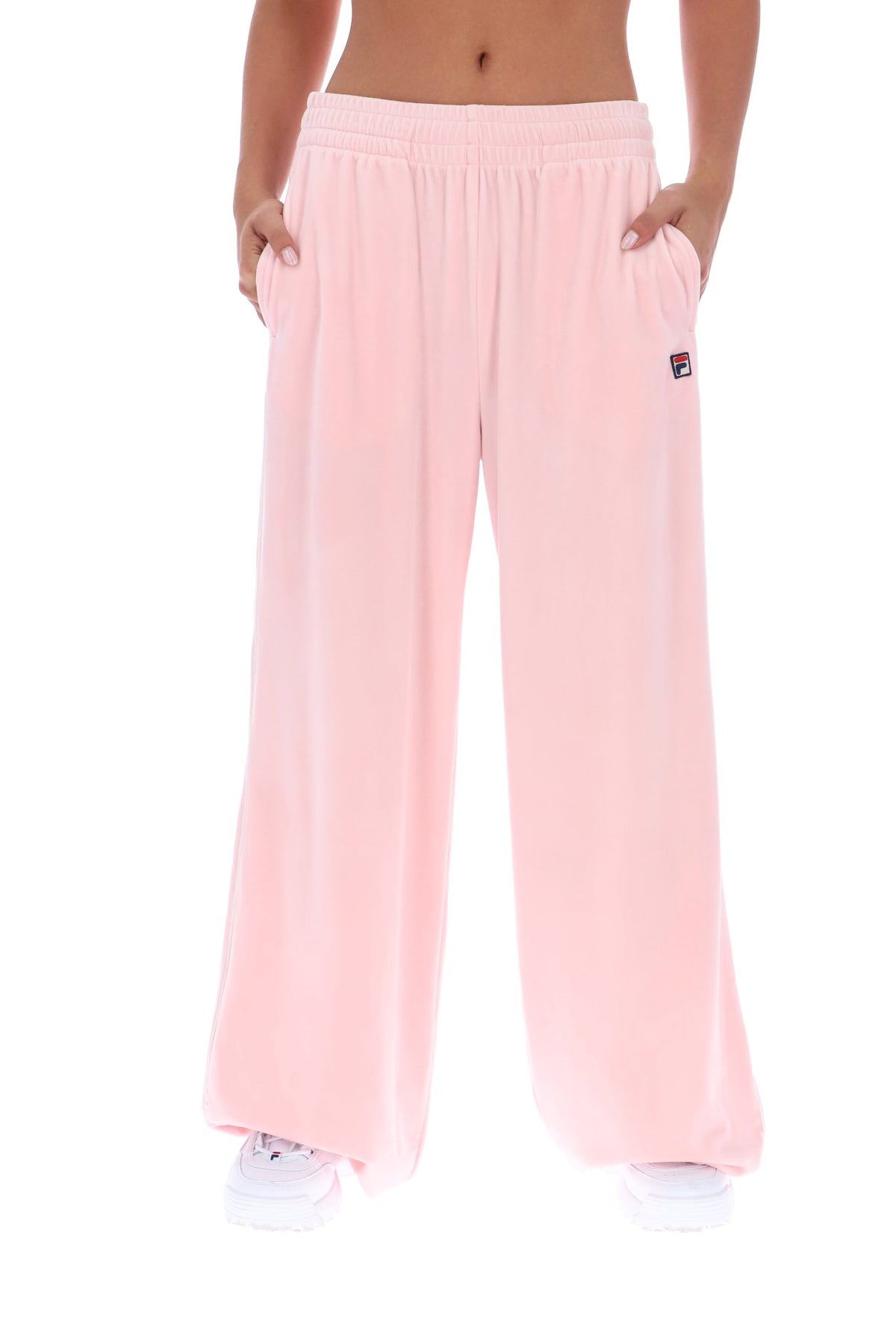 A person wearing light pink wide-leg sweatpants with side pockets and a small Fila logo patch on the left hip, shown against a plain white background.