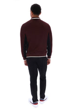 A man viewed from behind wearing a burgundy and black long-sleeve knit sweater with white trim, black pants, and white sneakers, shot against a plain white background.