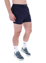 A person wearing black Artoni Swim Shorts with a drawstring waistband and the FILA logo on the leg, paired with white socks and grey sneakers.