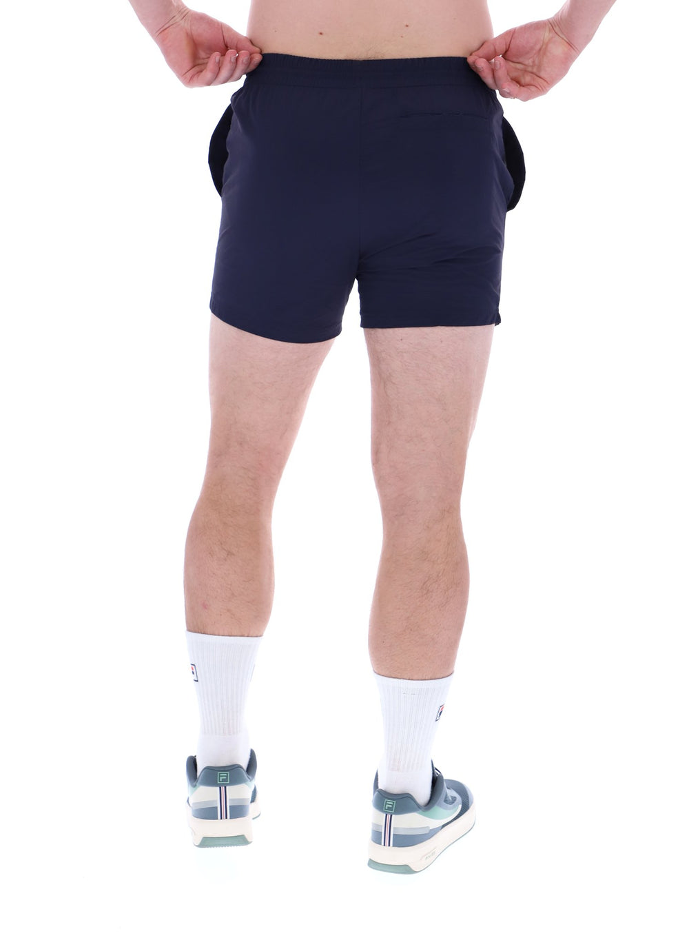 A person wearing black Artoni Swim Shorts with a drawstring waistband and the FILA logo on the leg, paired with white socks and grey sneakers.