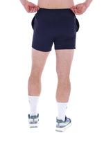 A person wearing black Artoni Swim Shorts with a drawstring waistband and the FILA logo on the leg, paired with white socks and grey sneakers.