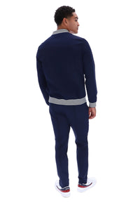 A man wearing a navy blue knit tracksuit with striped ribbed trim on the collar, cuffs, and hem, shown from the back against a plain white background.