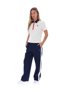 A woman modeling a matching Fila tracksuit set, featuring a white short-sleeve polo shirt with thin navy vertical pinstripes and a red zipper, paired with navy blue wide-leg sweatpants with white side stripes.