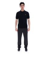 Man wearing a black polo shirt with a small FILA logo on the chest, paired with black FILA joggers, against a white background