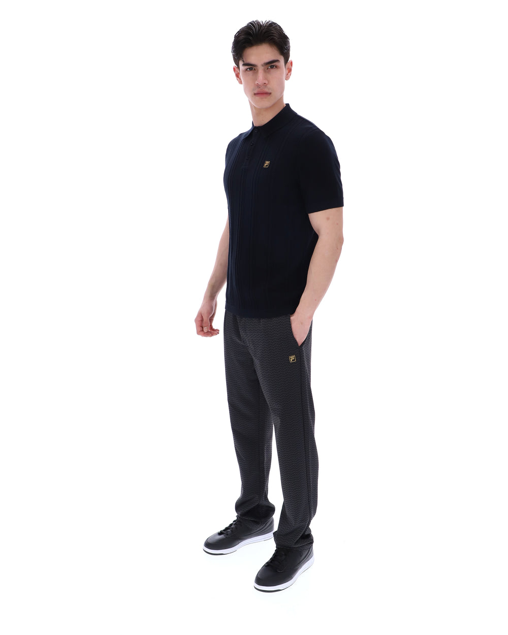 Man wearing a black polo shirt with a small FILA logo on the chest, paired with black FILA joggers, against a white background