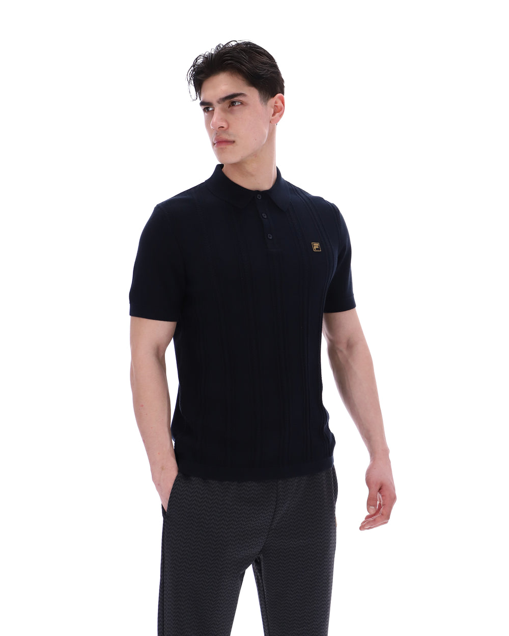 Man wearing a black polo shirt with a small FILA logo on the chest, paired with black FILA joggers, against a white background