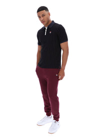 Man wearing a dark pinstripe polo shirt and maroon pants with a FILA logo on both, on a white background