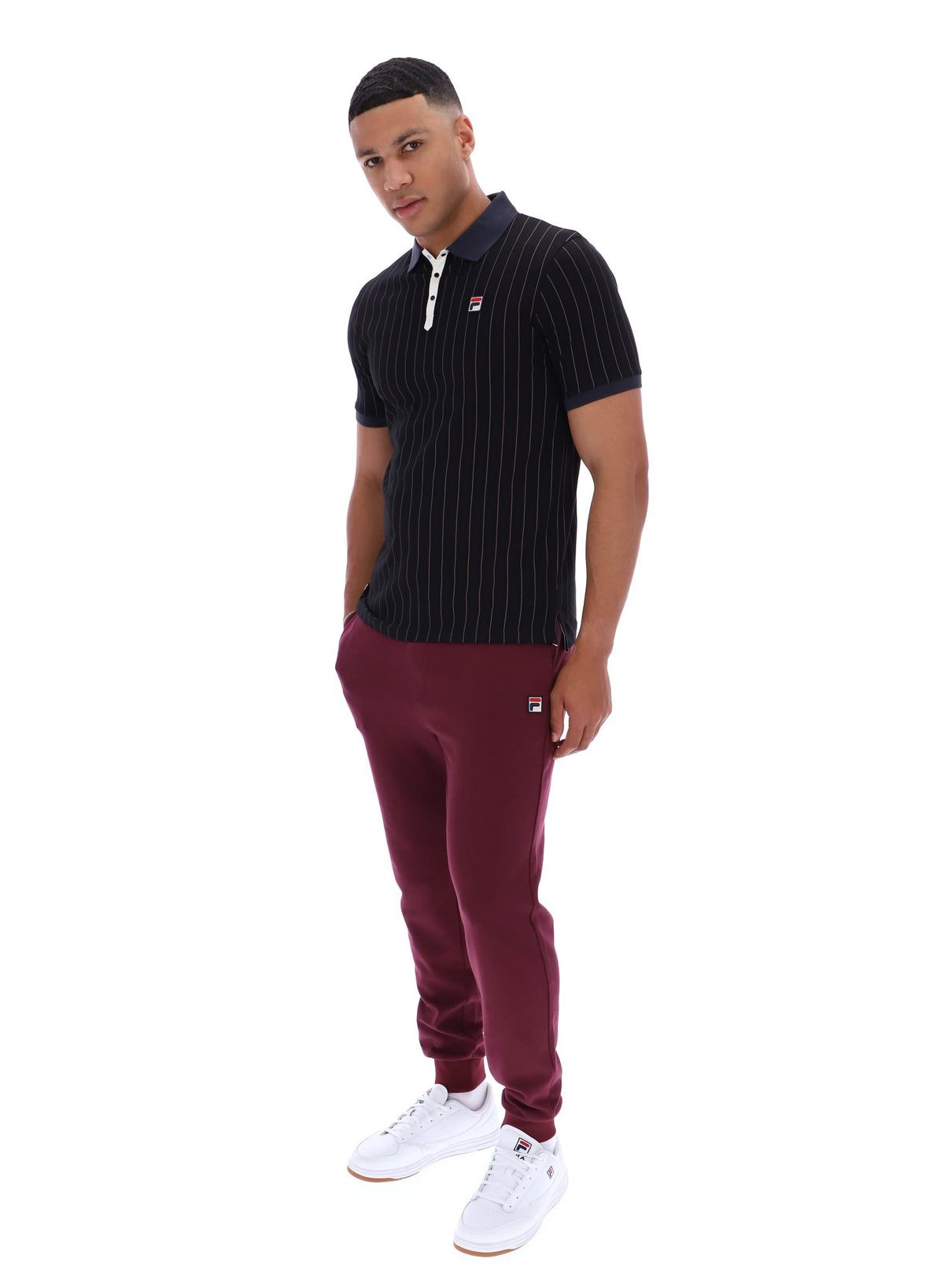 Man wearing a dark pinstripe polo shirt and maroon pants with a FILA logo on both, on a white background