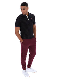 Man wearing a dark pinstripe polo shirt and maroon pants with a FILA logo on both, on a white background