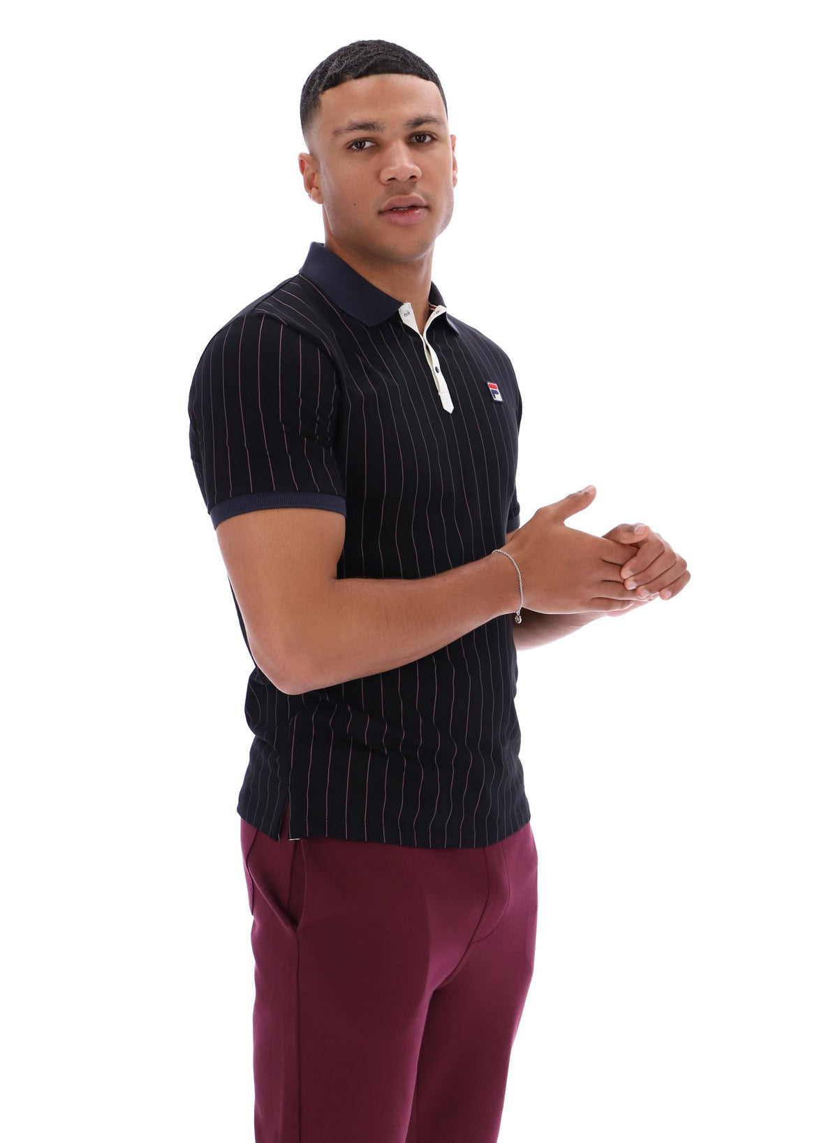 Man wearing a dark pinstripe polo shirt and maroon pants with a FILA logo on both, on a white background