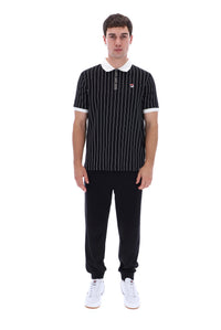 A man modeling a black short-sleeve polo shirt with thin white vertical pinstripes, a white collar, and a small red and white logo on the left chest, paired with black pants and white sneakers against a plain white background.