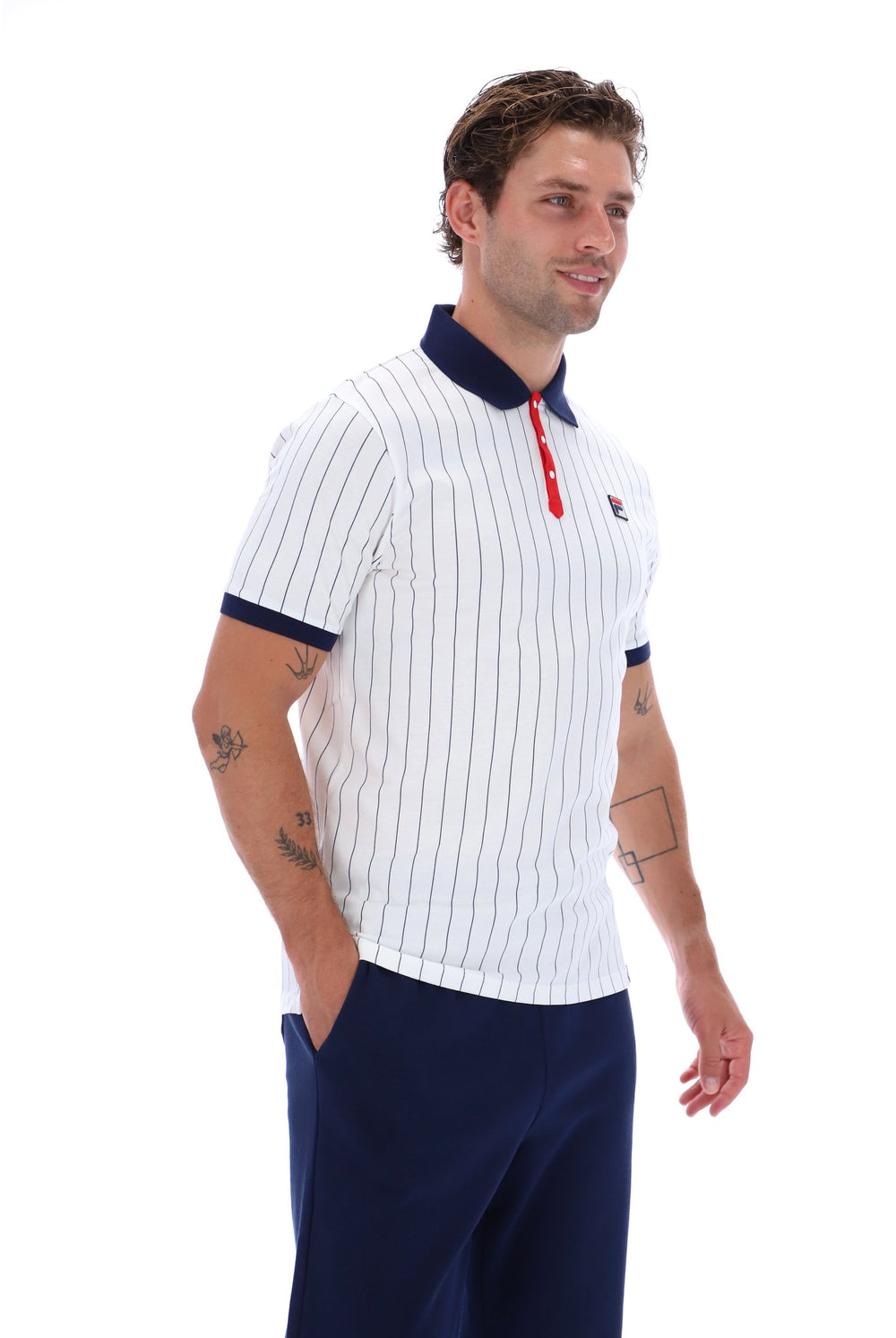 A man wearing a white short-sleeve polo shirt with thin navy vertical pinstripes, a navy collar, and a red button placket, paired with navy pants, against a plain white background.