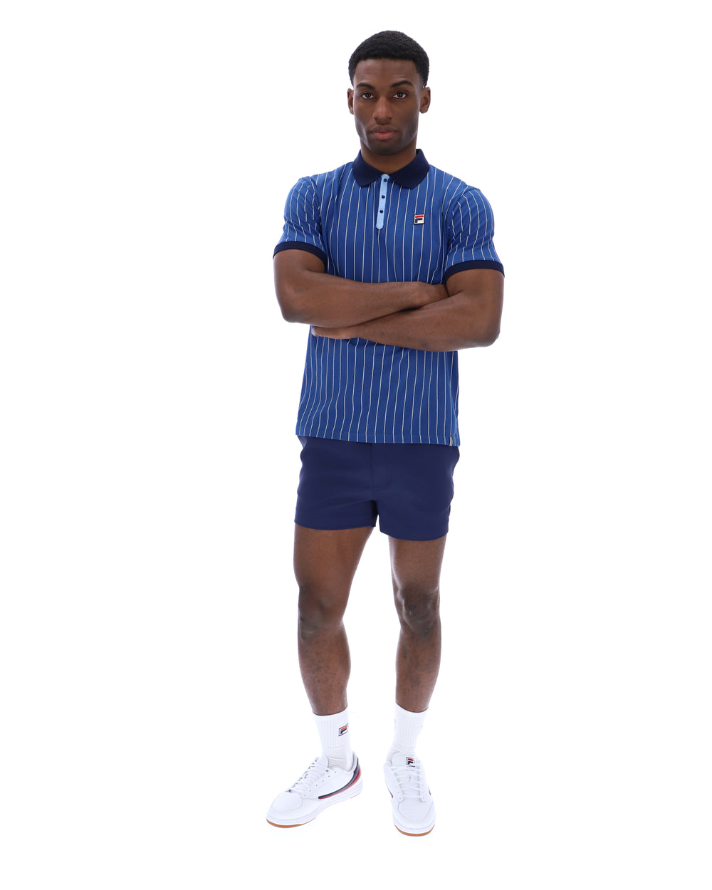 Man wearing a blue striped polo shirt and shorts with white socks and shoes on a white background