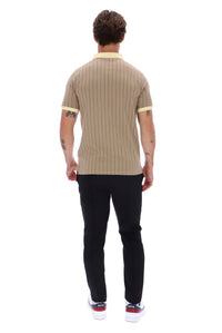 A man viewed from behind wearing a beige short-sleeve knit polo shirt with thin vertical black pinstripes and light yellow collar and sleeve trim, paired with black pants and white sneakers.
