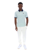 Man wearing a striped polo shirt and white pants on a white background