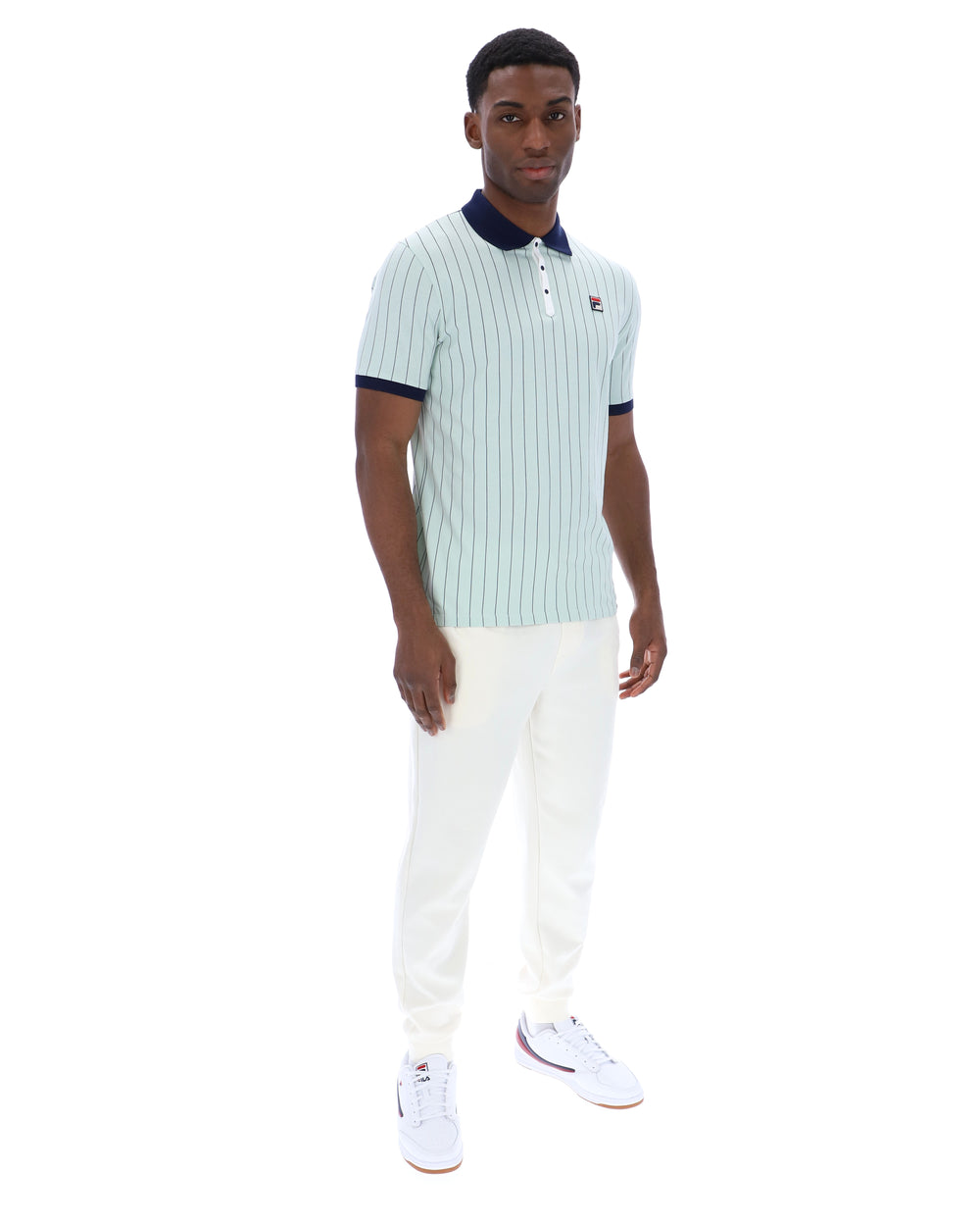 Man wearing a light blue striped polo shirt and white pants on a white background