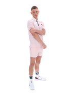 Man wearing a light pink polo shirt and shorts set with white shoes on a white background