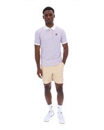 Man wearing a light purple polo shirt and beige shorts on a white background