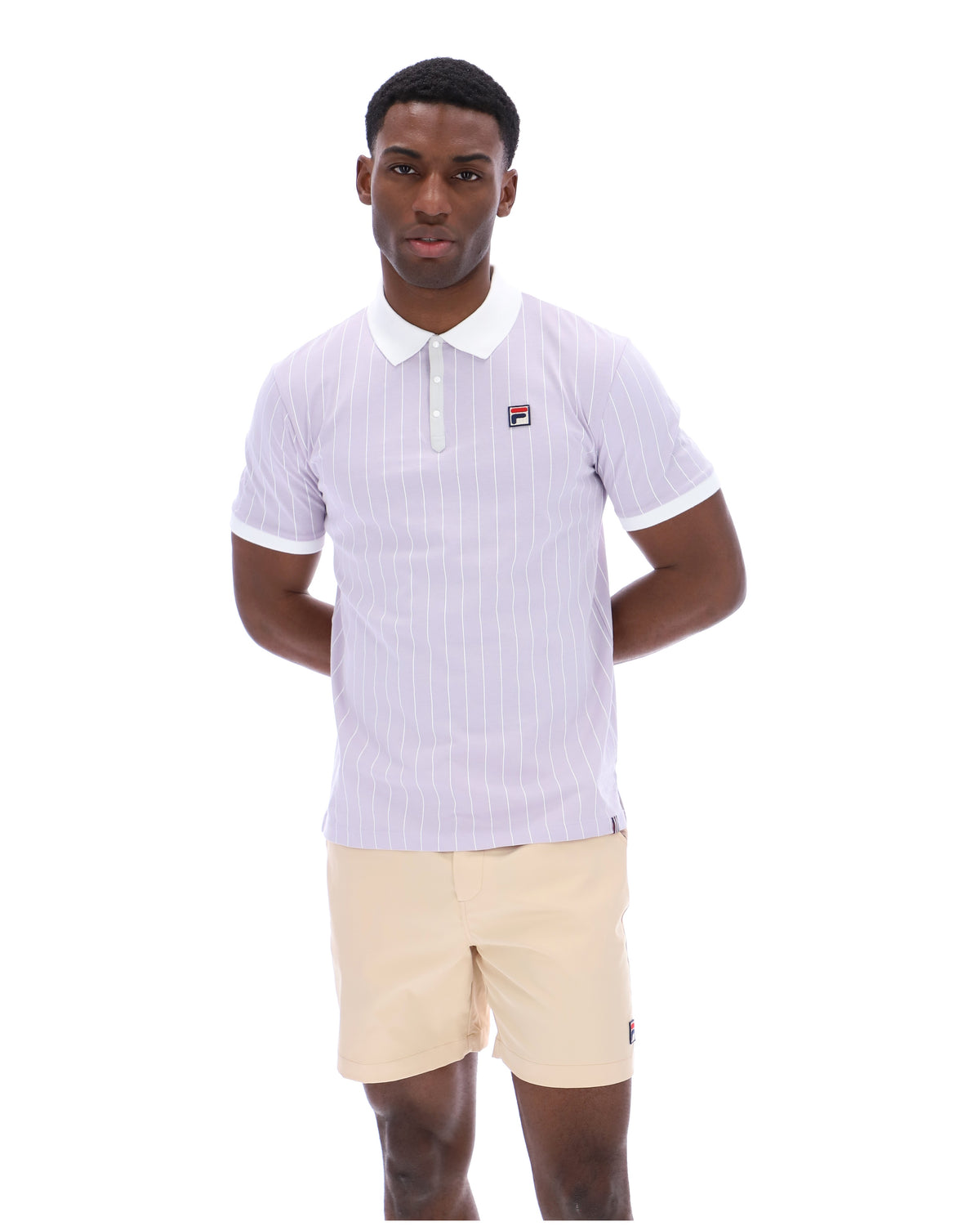 Man wearing a lilac striped polo shirt with a FILA logo on the chest, paired with beige shorts on a white background