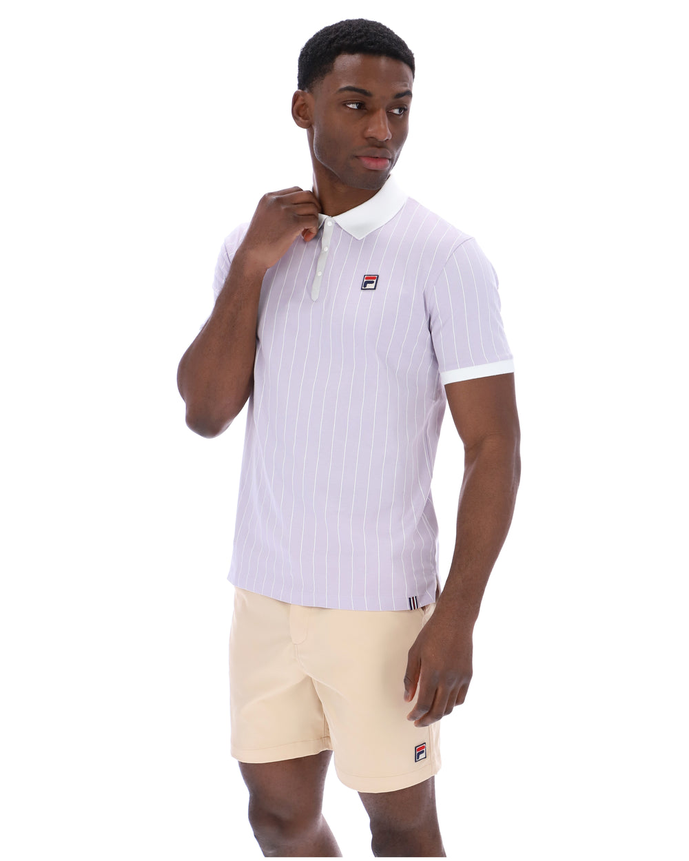 Man wearing a lilac striped polo shirt with a FILA logo on the chest, paired with beige shorts on a white background