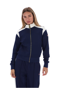 A woman modeling a navy blue and white track jacket with a gold zipper, paired with matching navy pants, against a plain white background.
