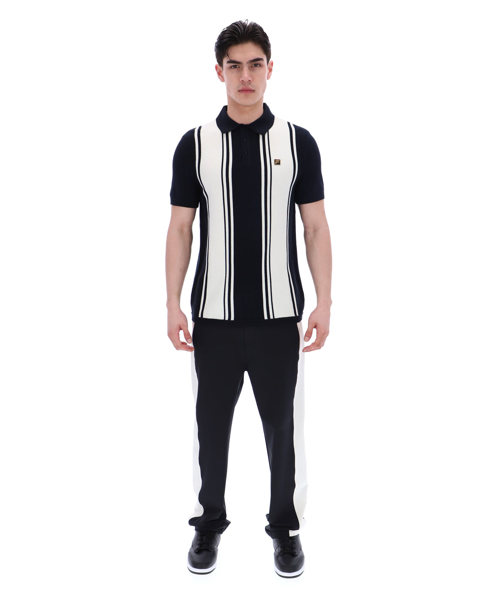 Person wearing a black and white striped shirt with a FILA logo on the chest and black pants on a white background