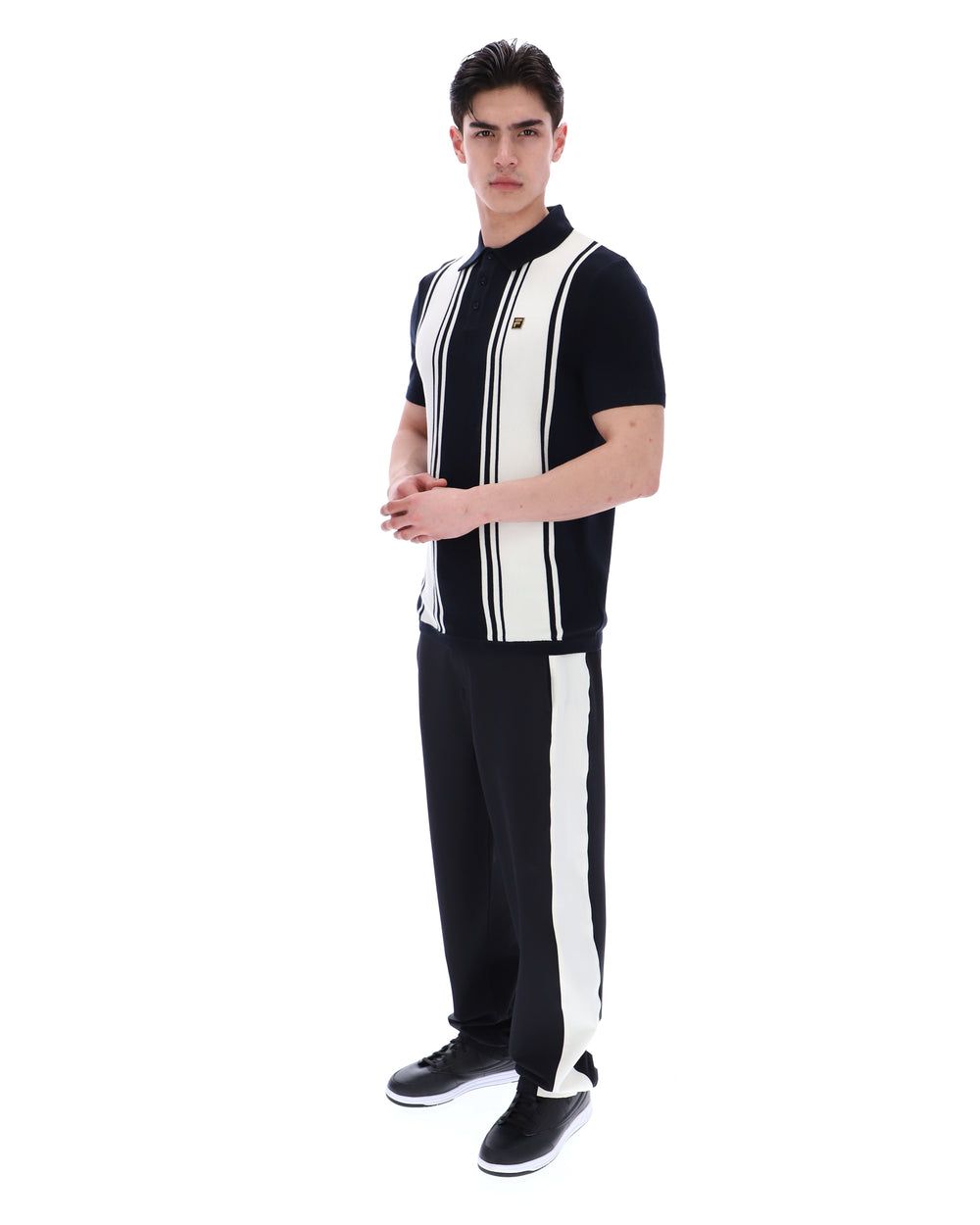 Person wearing a black and white striped shirt with a FILA logo on the chest and black pants on a white background