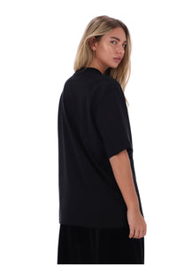 A woman with blonde hair is shown from a side-back angle wearing an oversized black short-sleeve top and matching black bottoms against a plain white background.