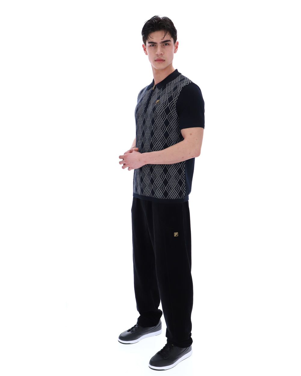Man wearing a black and grey patterned shirt with black pants on a white background