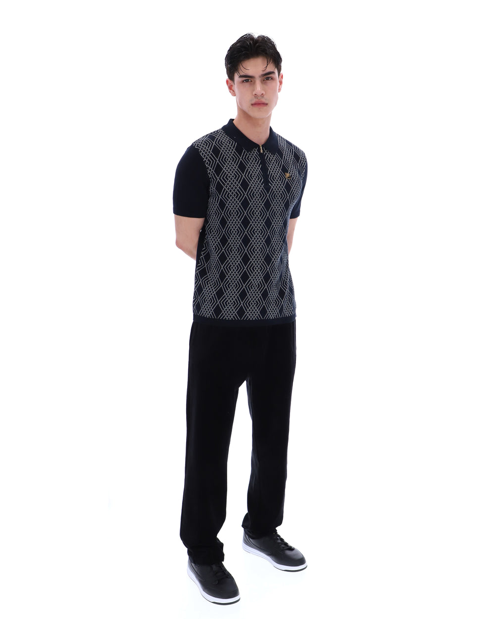 Man wearing a patterned vest over a black shirt with black pants on a white background