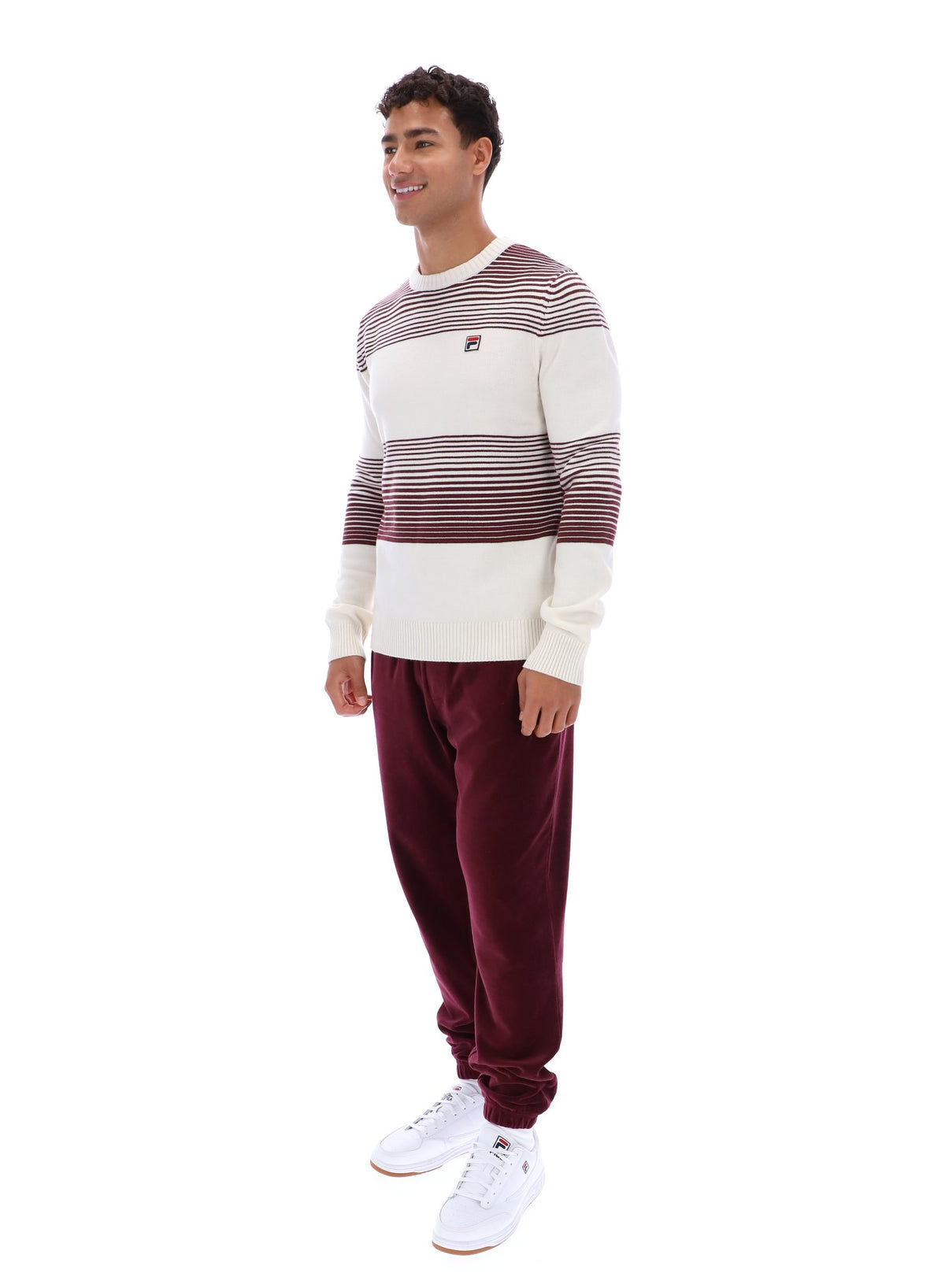 Man wearing a striped sweater and burgundy pants on a white background