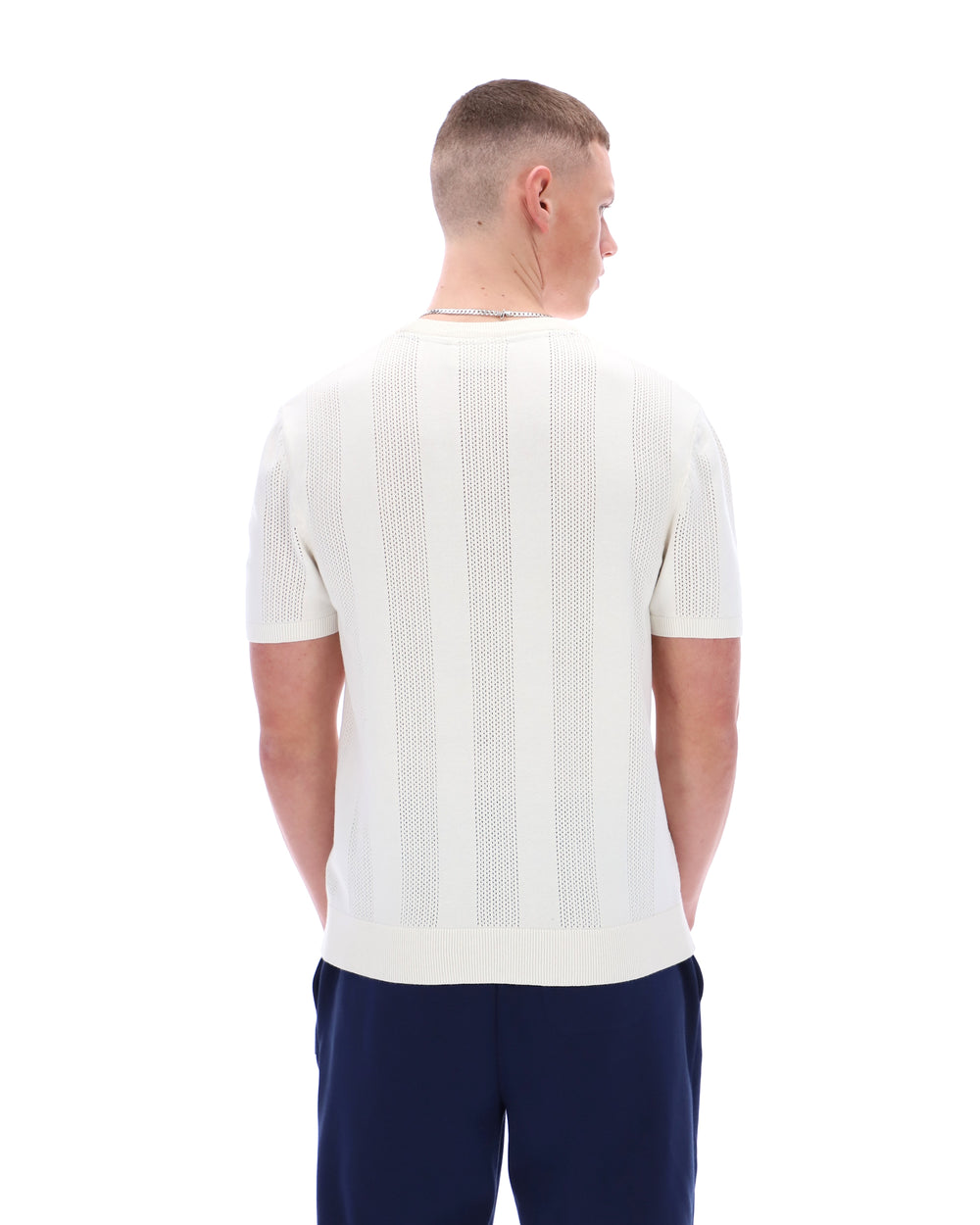 Man wearing a white textured shirt and dark pants on a white background