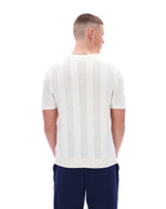 Man wearing a white textured shirt and dark pants on a white background