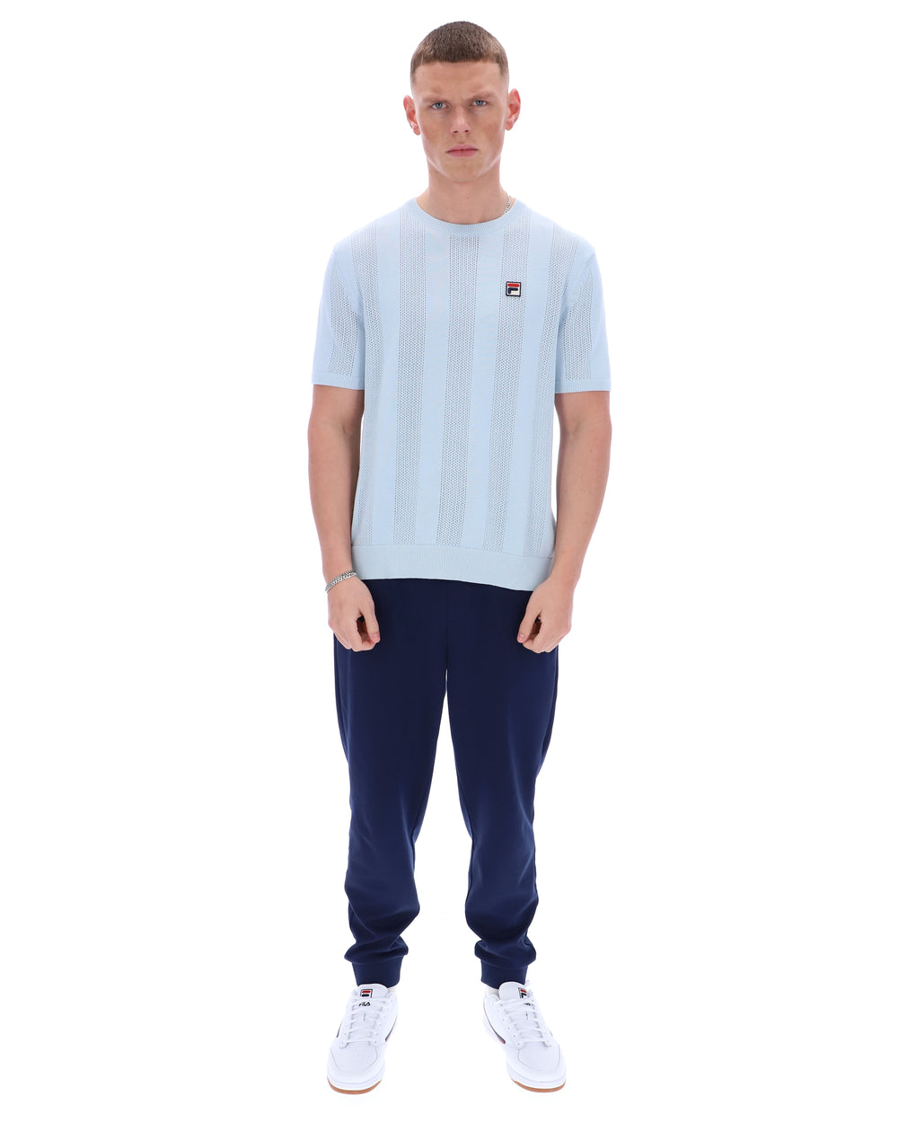Man wearing a light blue t-shirt and navy tracksuit pants on a white background